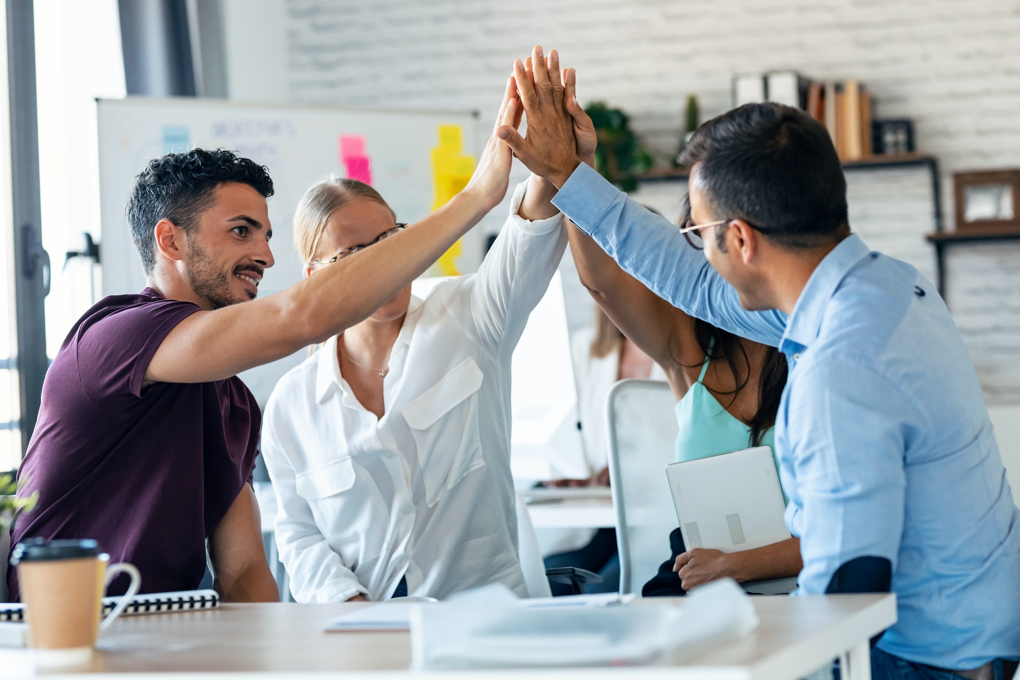 Successful business team celebrating good job while holding up their right hands on coworking place.