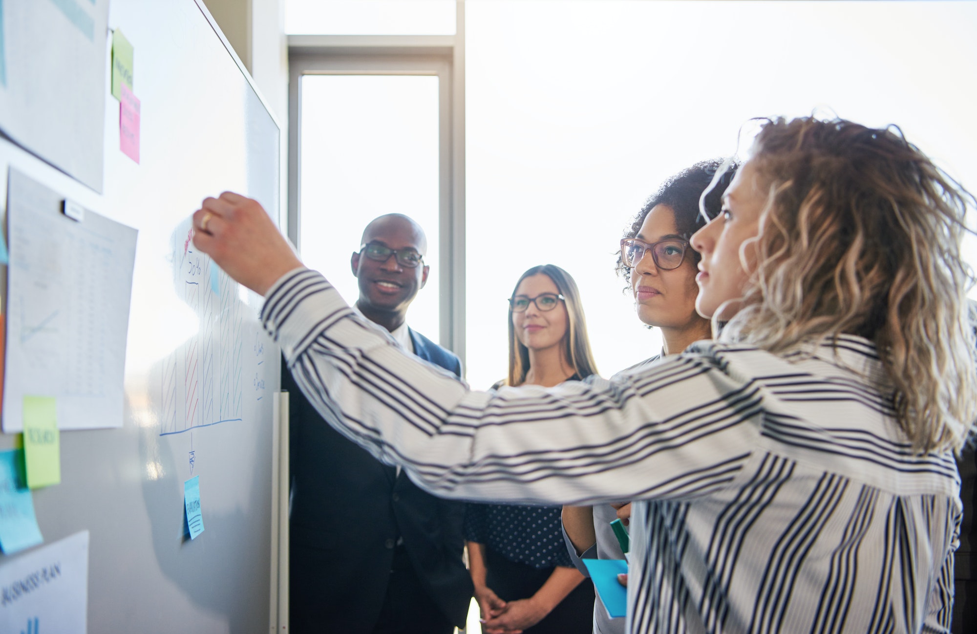 Coworkers strategizing together on a whiteboard in an office